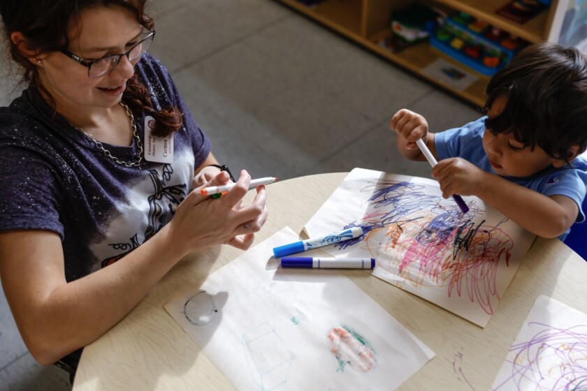 A child care worker colors with a child at a table