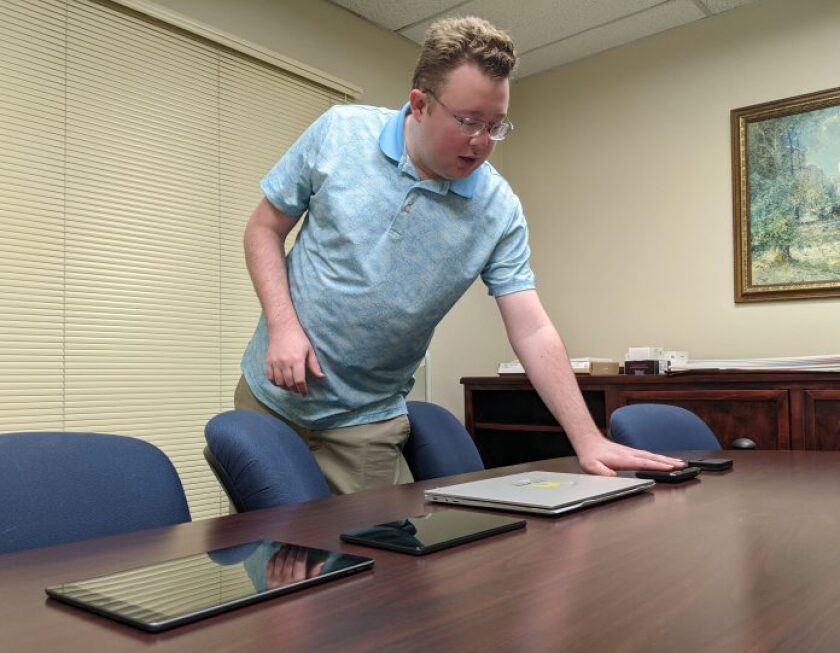 Ector County Library's IT administrator, in blue polo, shows recently purchased mobile devices, laid out on a table.