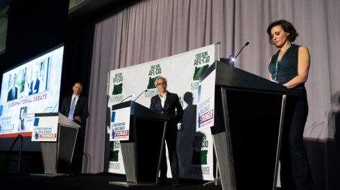 Three people stand at podiums during a political debate