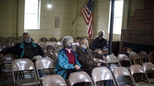 two people sit with masks on metal folding chairs in Pelham's Town Hall