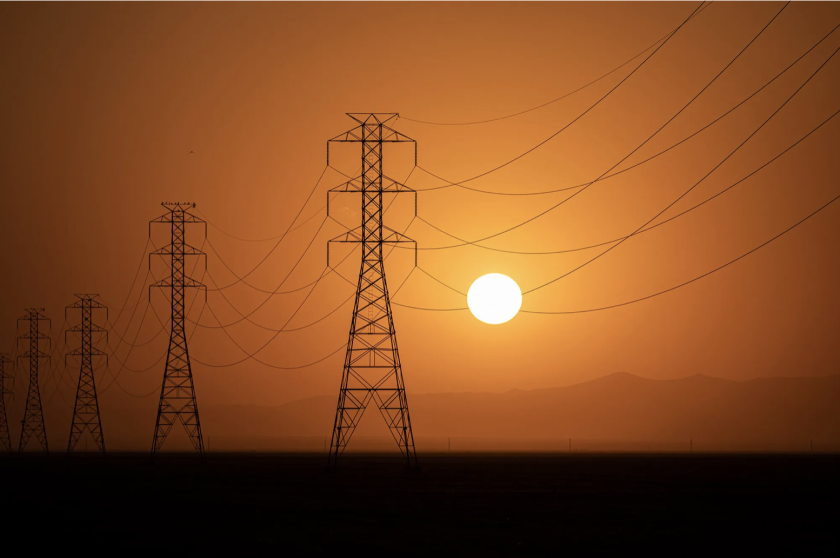 The sun sets behind a row of transmission towers
