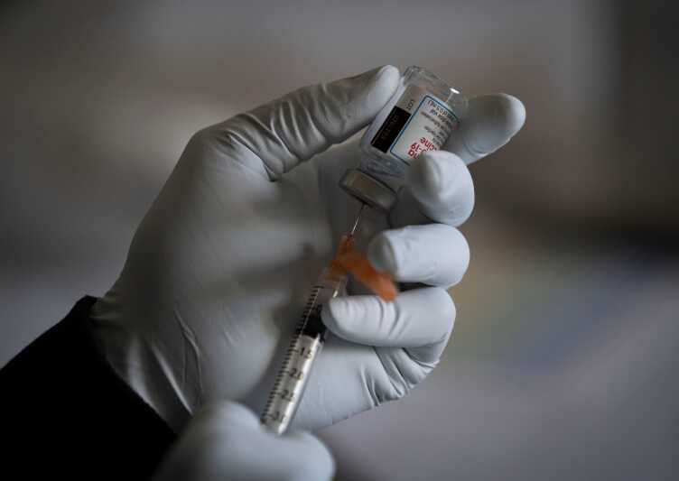 Closeup of a pair of gloved hands preparing a dose of a vaccine.