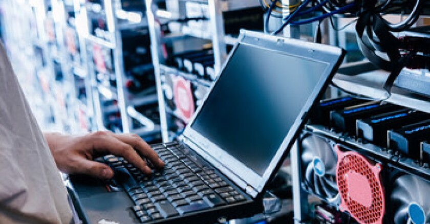 A person standing in a data center working on a laptop.