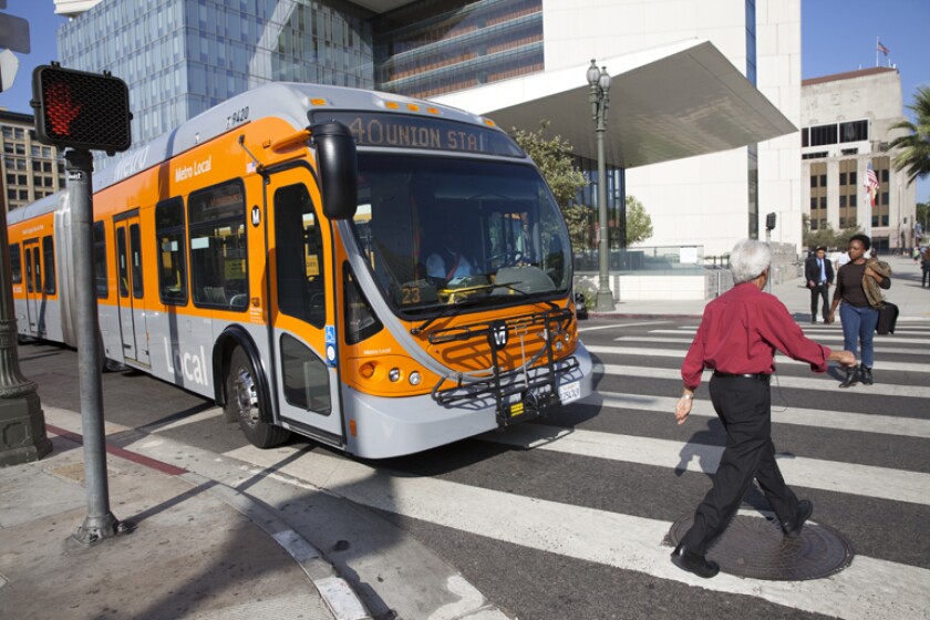 People walking across the street while a bus waits.