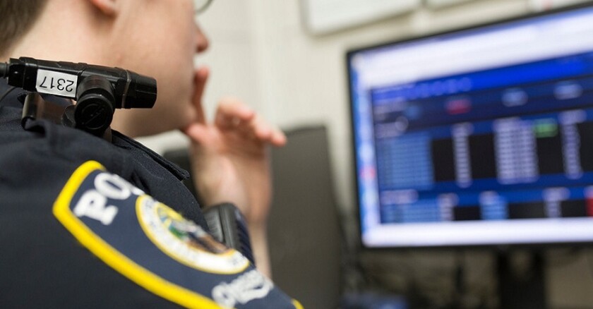 A police officer wearing a body camera sitting at a computer.