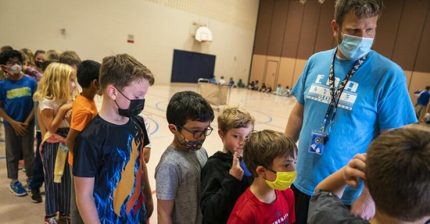 a man in a mask stands by children in masks in a line