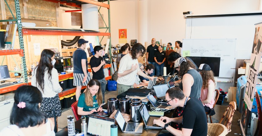 Participants at the Brooklyn Laptop Fix-a-thon work to refurbish laptops to support community digital literacy programming. A group of people sit around working on fixing laptops at the Brooklyn Spark Makerspace.