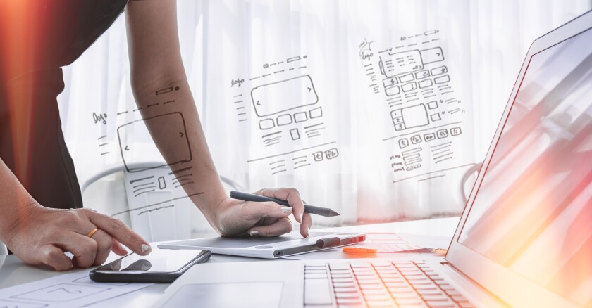 A person working on a smartphone and a notepad at a desk. In front of them is an open laptop.