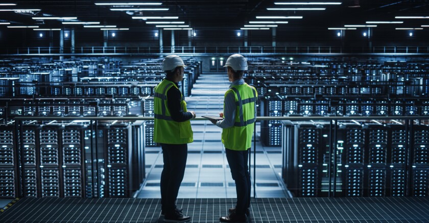 Two employees, one holding a tablet, talk together in a data center.