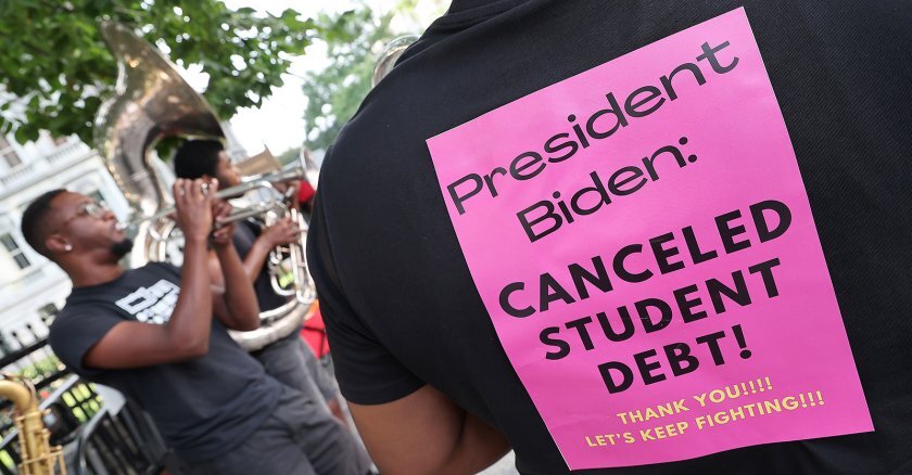 A pink piece of paper stuck to the back of a person’s shirt that reads “President Biden: canceled student debt! Thank you!!!! Let’s Keep Fighting!!!”