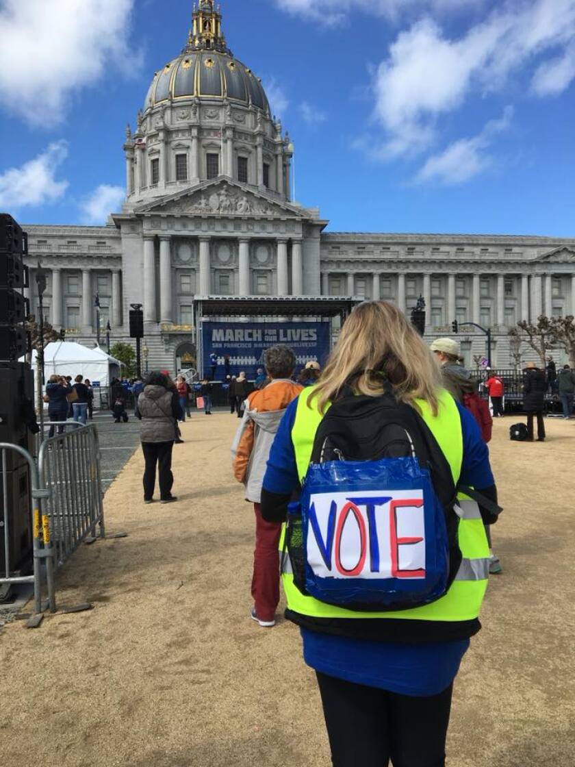 A person at a gun control rally in San Francisco with the word "VOTE" in large letters on the back of their backpack.