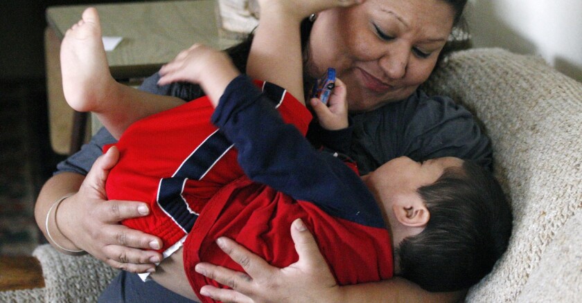 Latina woman cradles a toddler while sitting on the couch.