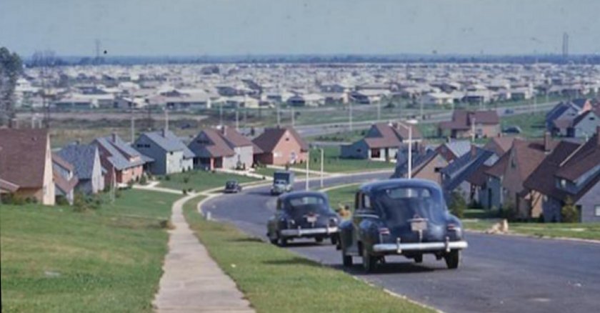 Cars driving down the street in a postwar suburb following World War II.
