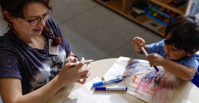 A child care worker colors with a child at a table