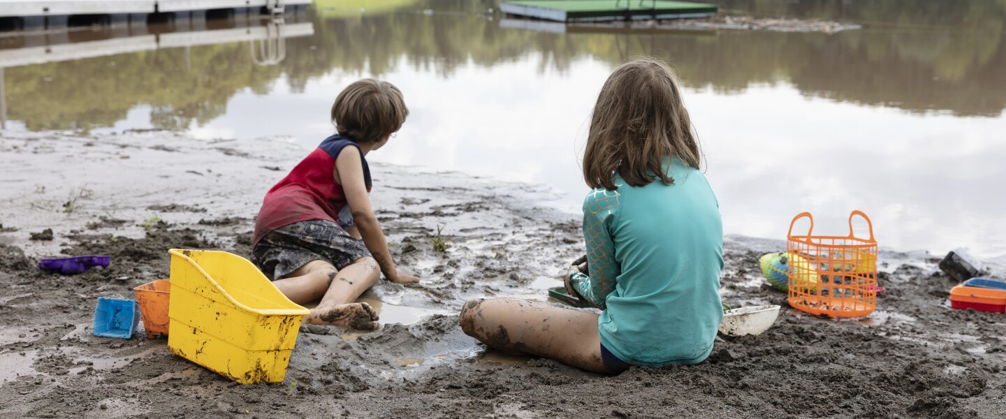 Children playing in the mud at the edge of a body of water.
