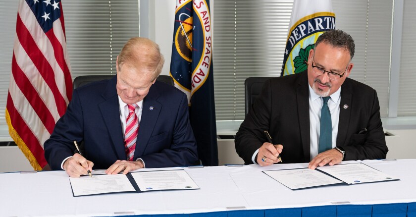 NASA Administrator Bill Nelson and Secretary of Education Miguel Cardona sitting side-by-side signing papers.