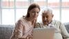 Older adult and younger adult sitting together looking at a laptop computer sitting on a table.