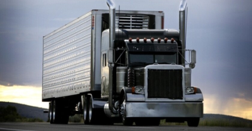 A semitruck on a road with a cloudy sky in the background.