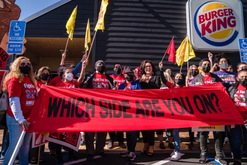 people standing in front of a Burger King with a banner that reads "Which Side Are You On?"