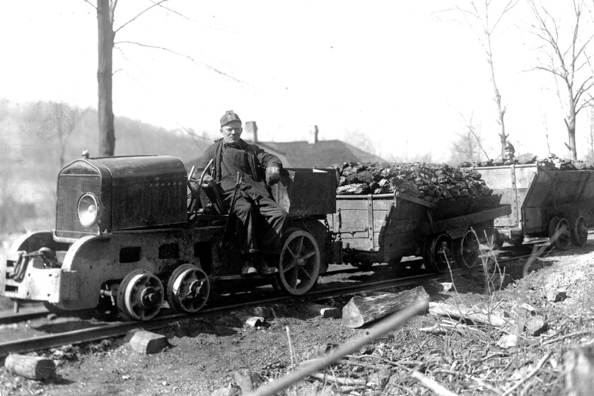 A black and white image of a man sitting on a small locomotive used in coal mines.