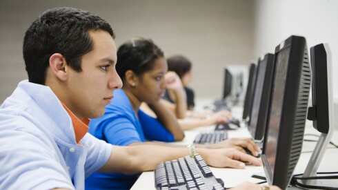 A row of students working on desktop computers in a computer lab.