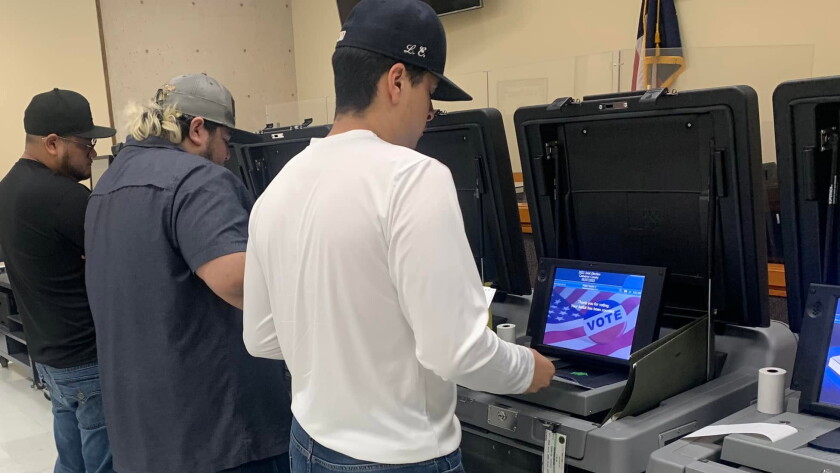 Three people standing in front of machines used for pre-election testing.