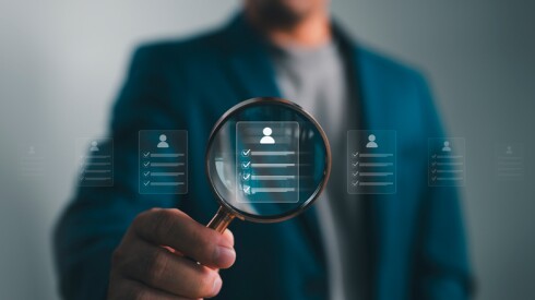 Person in a suit holding up a magnifying glass with a list inside