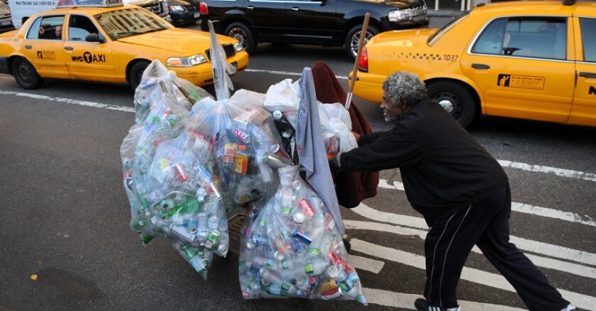Homeless man walking with shopping cart full of cans.