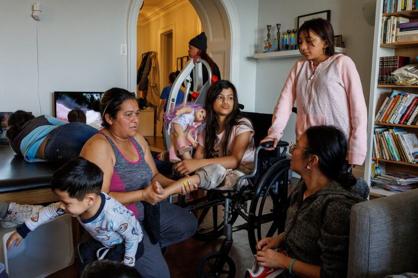 family members sit in a living room, one girl is in a wheelchair