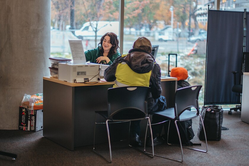 Hannah Chandler sitting behind a desk in the library working with a patron.