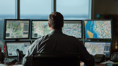 man sitting in front of eight computer screens showing location data and maps