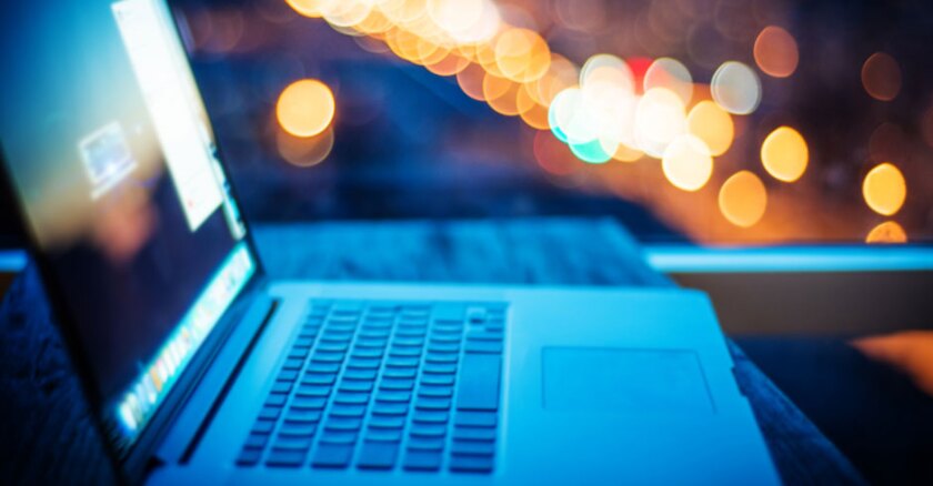 An open laptop seen from the side with blurred city lights in the background.