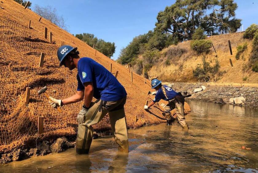 Corps members place erosion control mats on a stream bank.