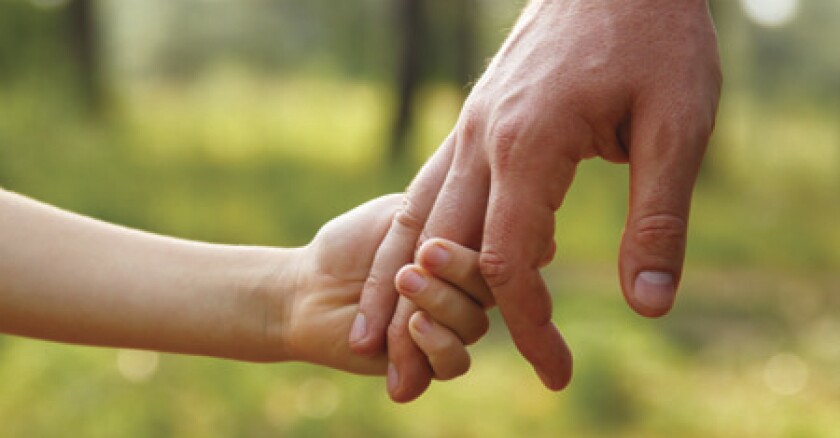 Closeup of a child's hand coming from the left side of the image and holding some of the fingers of an adult's hand coming from the right side of the image.