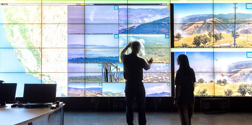 Two analysts look at screens of wildfire data from California