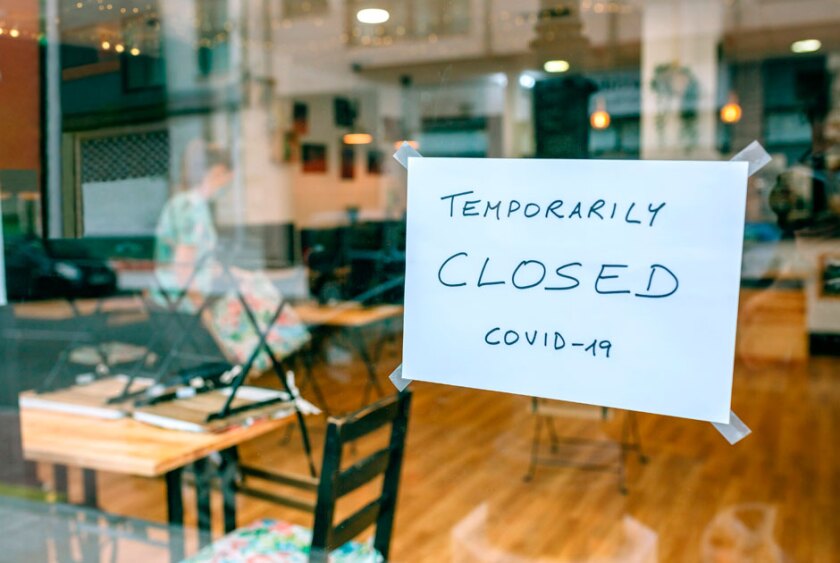 A+sign+taped+to+the+window+of+a+cafe+reads+%22temporarily+closed+COVID-19%22
