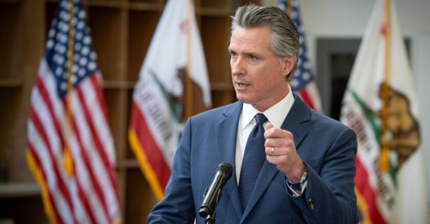 California Gov. Gavin Newsom standing behind a podium and speaking while gesturing with his left hand.
