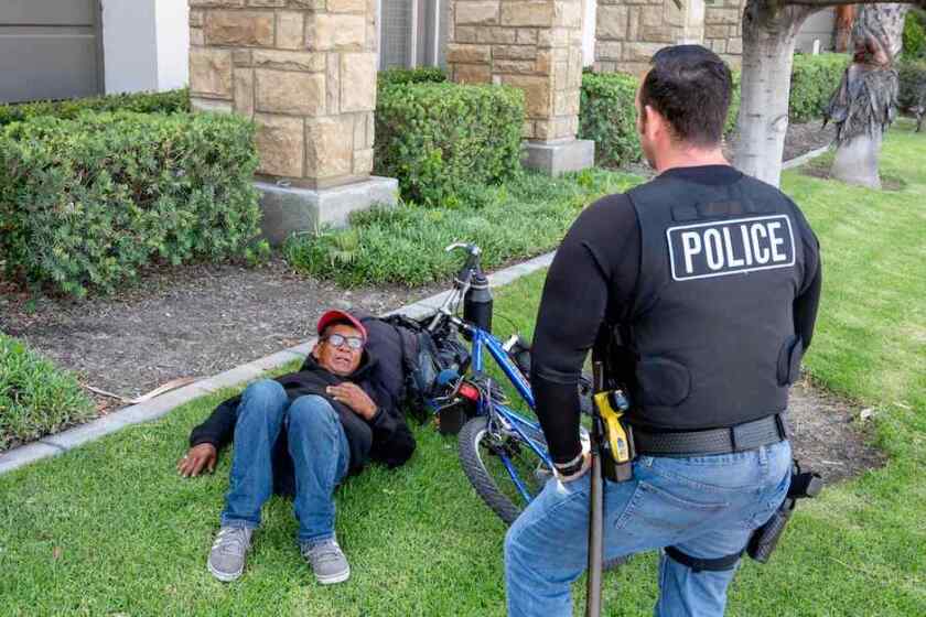 A police officer with the North Orange County, Calif., Public Safety Task Force speaking with a homeless person lying on the grass.