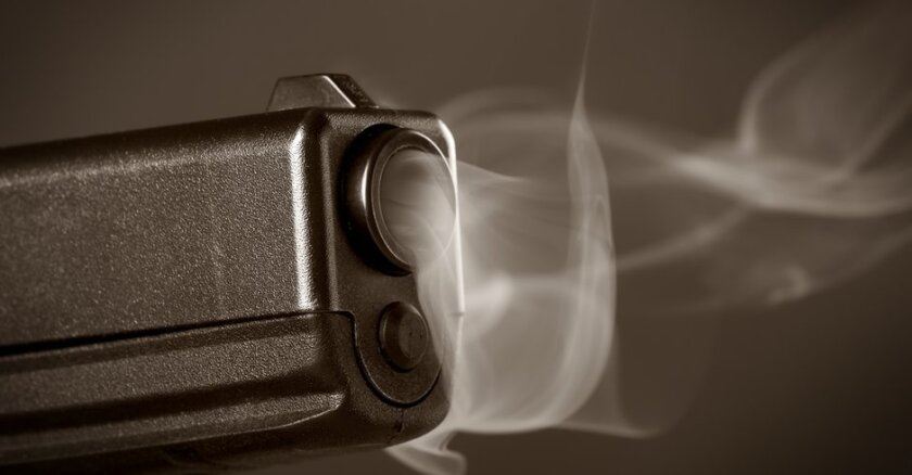 Closeup of the end of a pistol smoking after being fired.