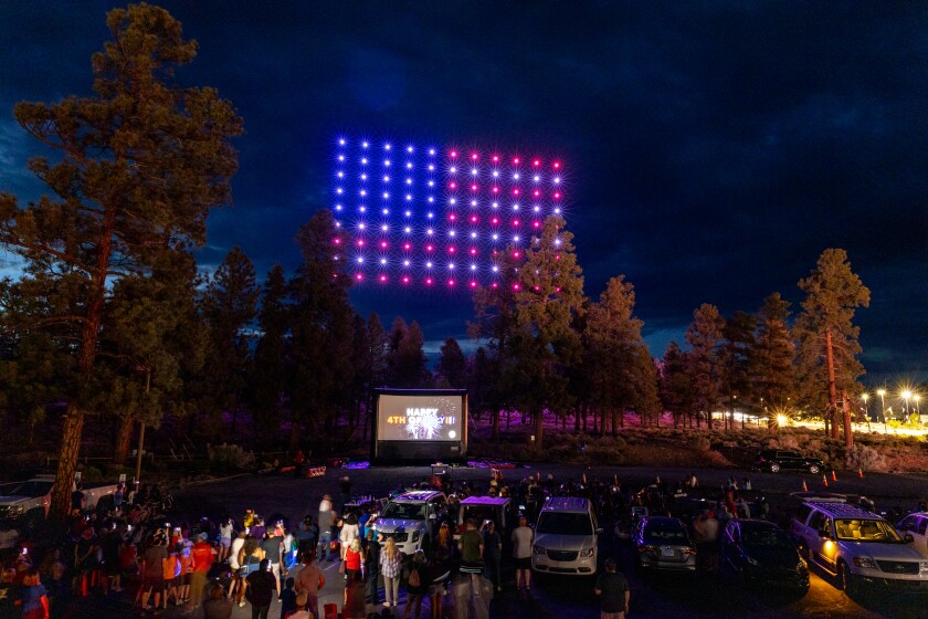 Drone show display shows an American flag as people stand around looking at it. A screen reads "Happy 4th of July!"