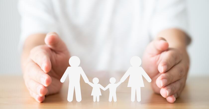 Hand protecting family on wood table. Healthcare and life insurance concept
