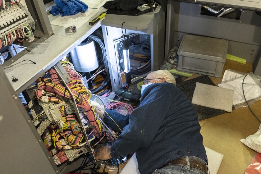 A man wearing a face masks laying on his side facing a large bundle of wires as he works on them.