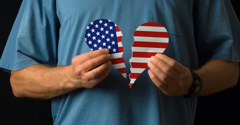 White man in button-up shirt holding a broken heart with the American flag on it,
