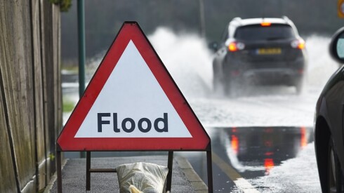 A sign that says "Flood" next to a flooded road.