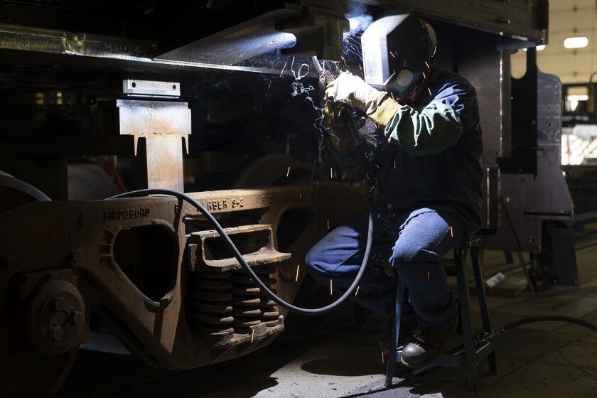 A technician wearing a welding mask while welding a part on a streetcar in the shop.