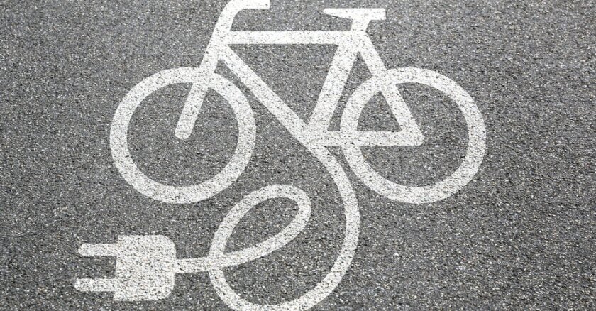 A digital drawing of a bike with an electric plug on pavement.