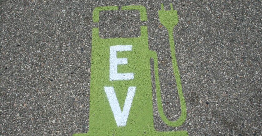 An electric vehicle charging station painted in green on asphalt, with the letters "EV" on it in white.