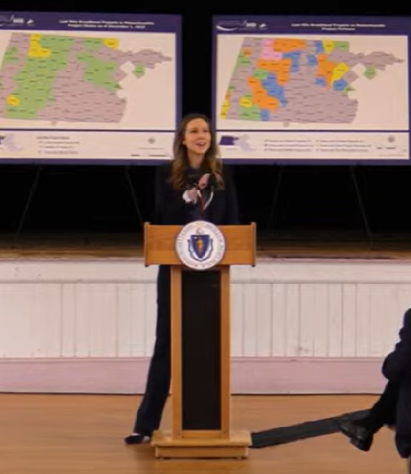 Ashley Stolba stands at podium before two broadband maps.