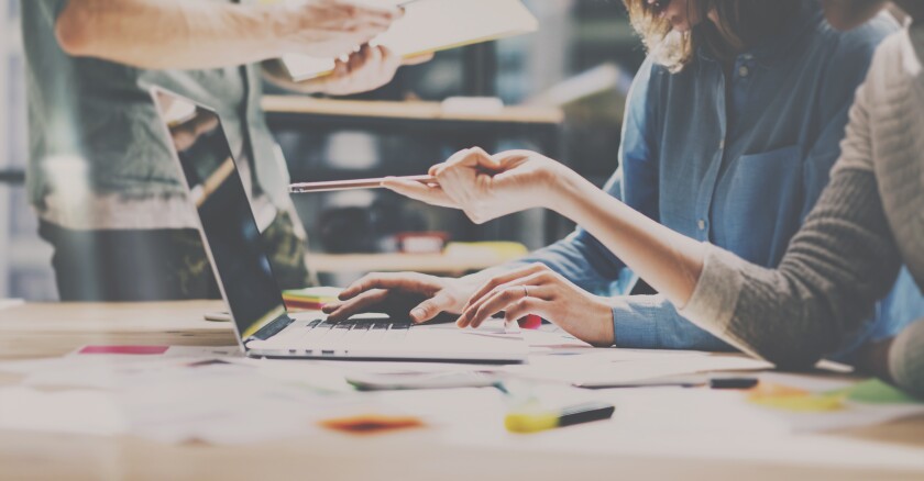 People sitting at a table working together on a laptop.
