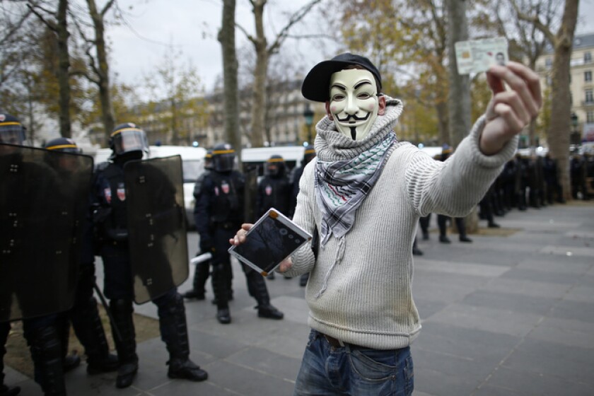 An anonymous activist wears a Guy Fawkes mask at a demonstration near French CRS police after the cancellation of a planned climate march following shootings in the French capital, ahead of the World Climate Change Conference 2015 (COP21), in Paris